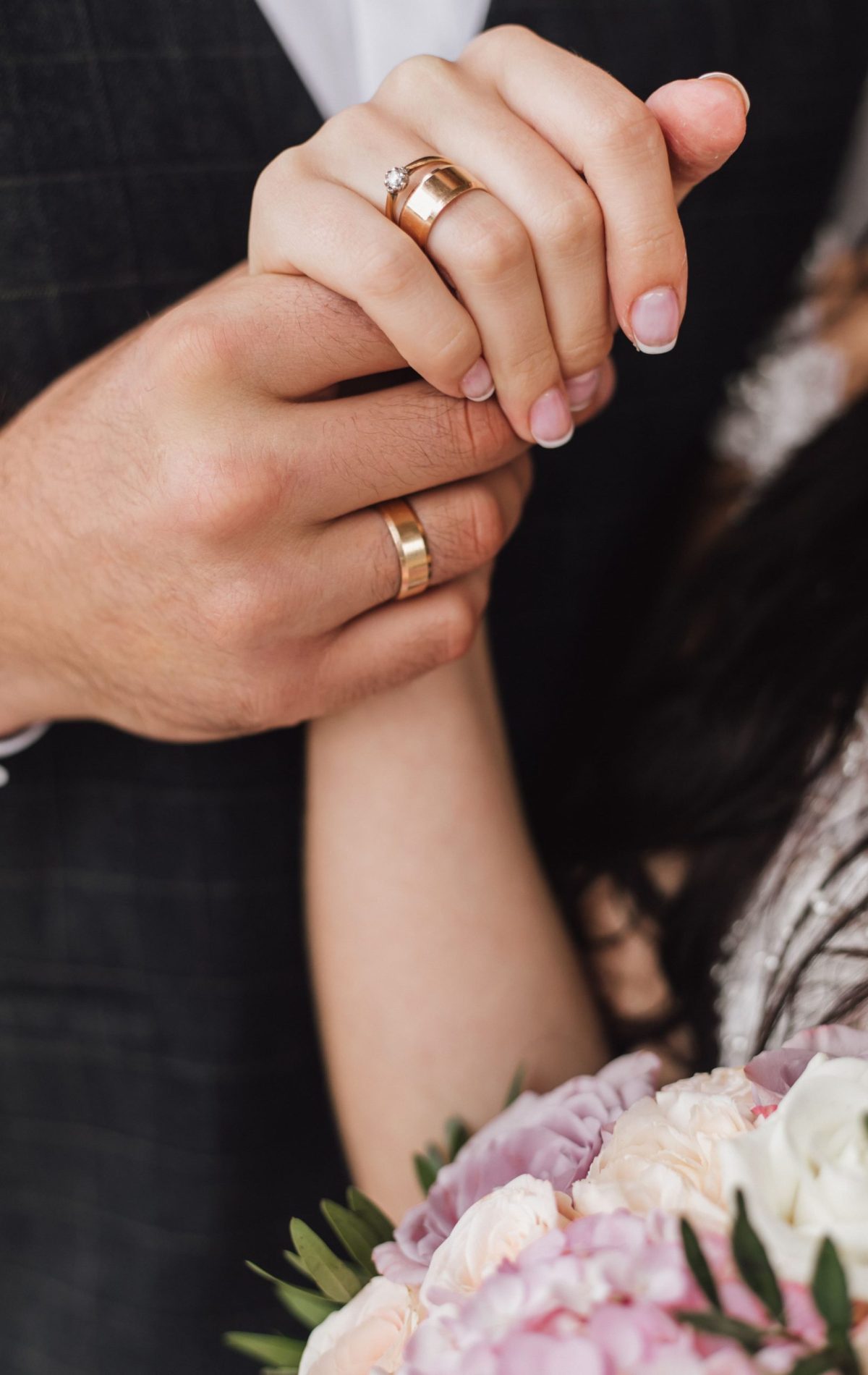 mani-di-una-moglie-e-un-marito-con-anelli-di-fidanzamento-e-matrimonio-e-parte-del-bouquet-floreale (1)